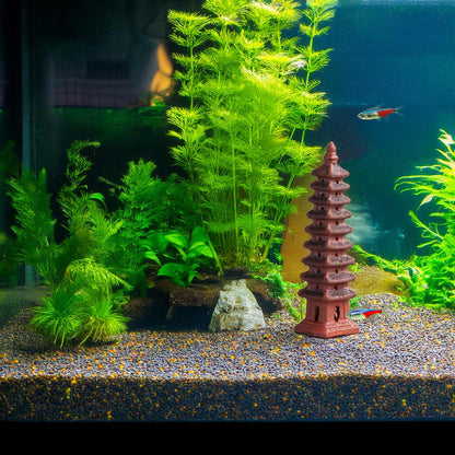 Nestled amongst vibrant green aquatic plants in a serene aquarium, a miniature ceramic pagoda adds a touch of tranquility to this underwater oasis.