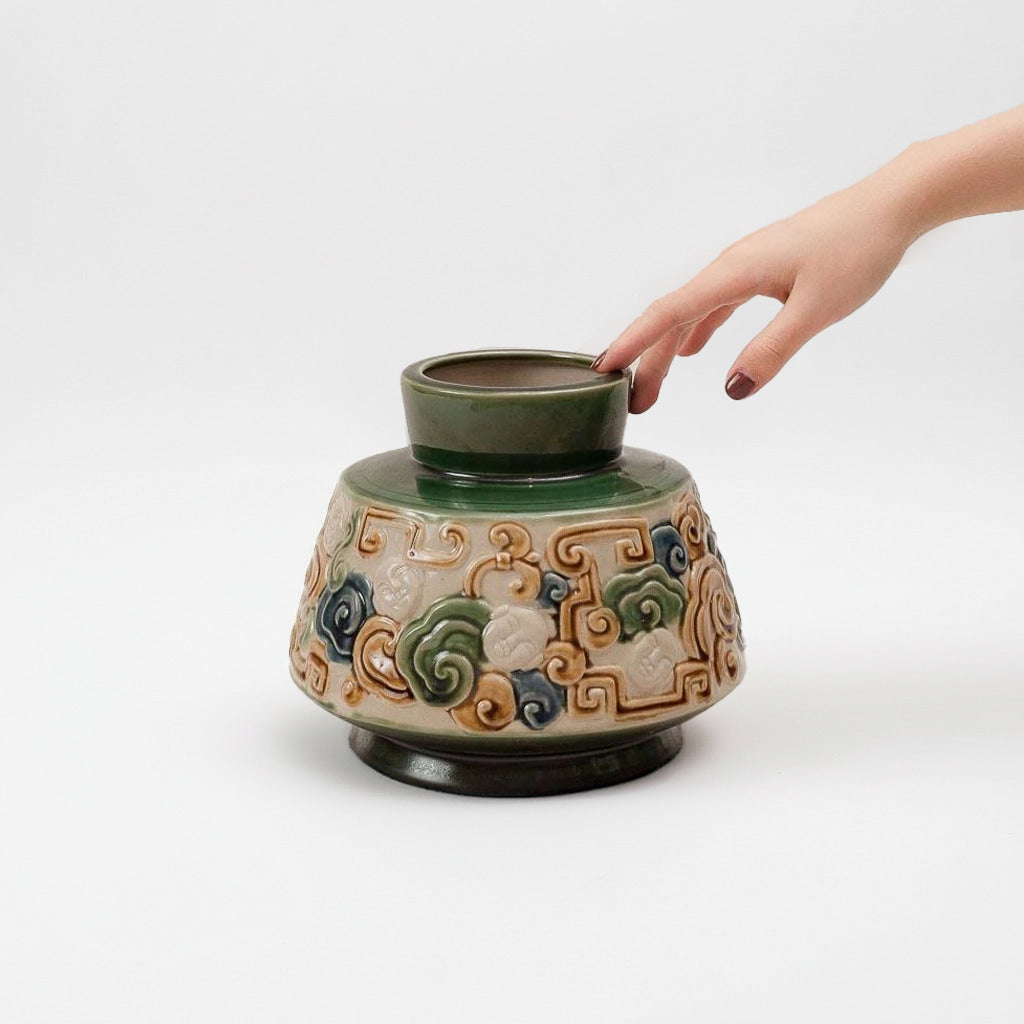A hand touches a handmade in Vietnam vase. This artisan vase is a low wide flower vase. 