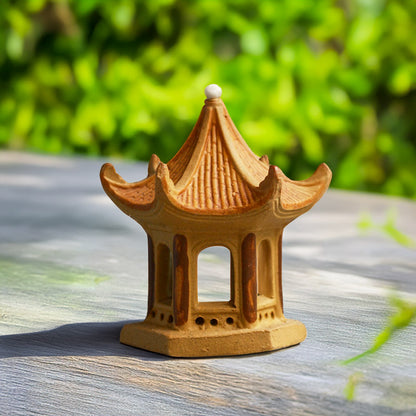 A miniature Vietnamese pagoda, crafted from earthy brown ceramic, stands serenely on a wooden surface, evoking a sense of tranquility and ancient beauty.