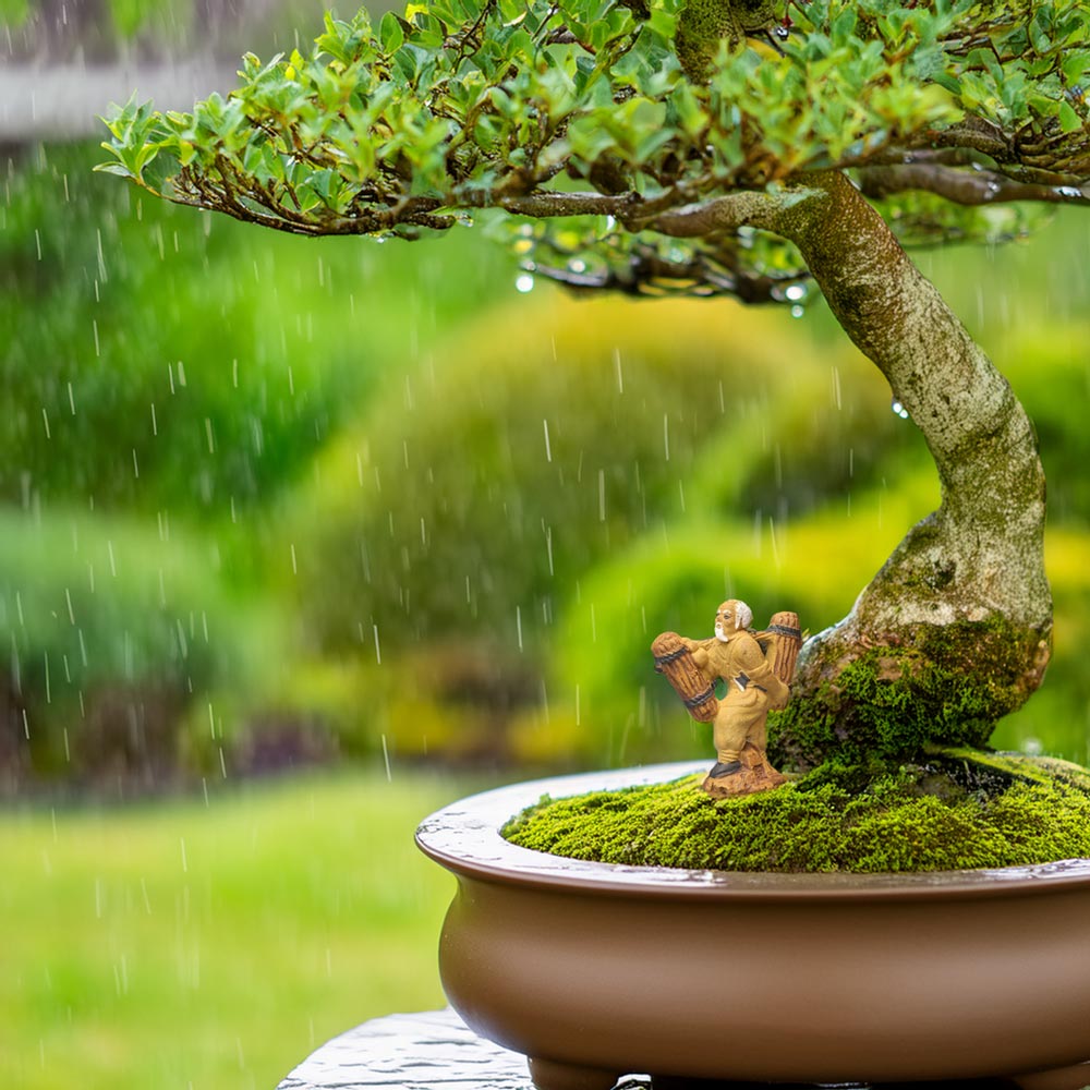 A small ceramic woodcutter stands on a moss-covered mound beneath a bonsai tree. It's raining in the background.