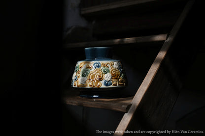 This blue Vietnamese ceramic vase with a raised cloud motif sits on a dark wooden shelf.