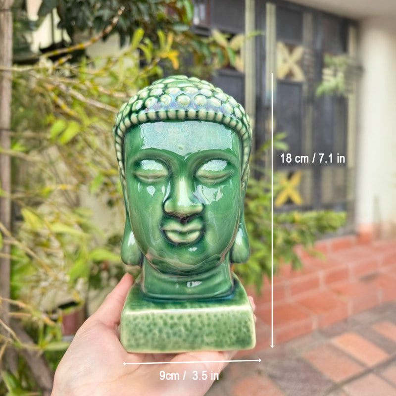 A hand holds a 7.1-inch tall buddha head statue green jade. An emerald buddha head statue.