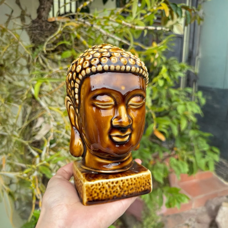 A hand holds a brown buddha head figurine. This is a buddha statue for good luck