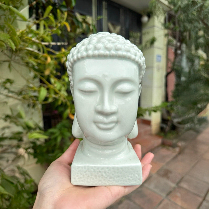  A hand holds a white buddha head statue. A unique piece for a peaceful buddha statue with bonsai.