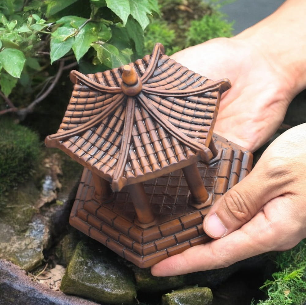 Two hands gently holding a brown ceramic hexagonal pavilion.