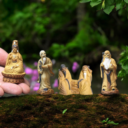 Four small ceramic mudmen figurines stand on a moss-covered surface.