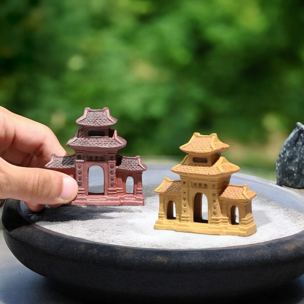 Two small ceramic three entrance gates, one brown and one yellow, stand on a bed of white sand.