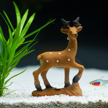 A brown ceramic deer figurine stands in an aquarium. This ceramic animal is on white sand.
