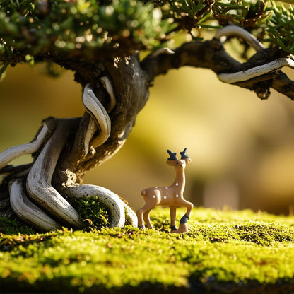 A small ceramic deer figurine stands on moss under a twisted bonsai tree. Fairy garden decor piece