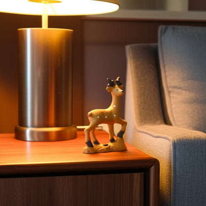 A brown ceramic deer figurine, a deer statue for home decor, sits on a wooden nightstand by a lamp.