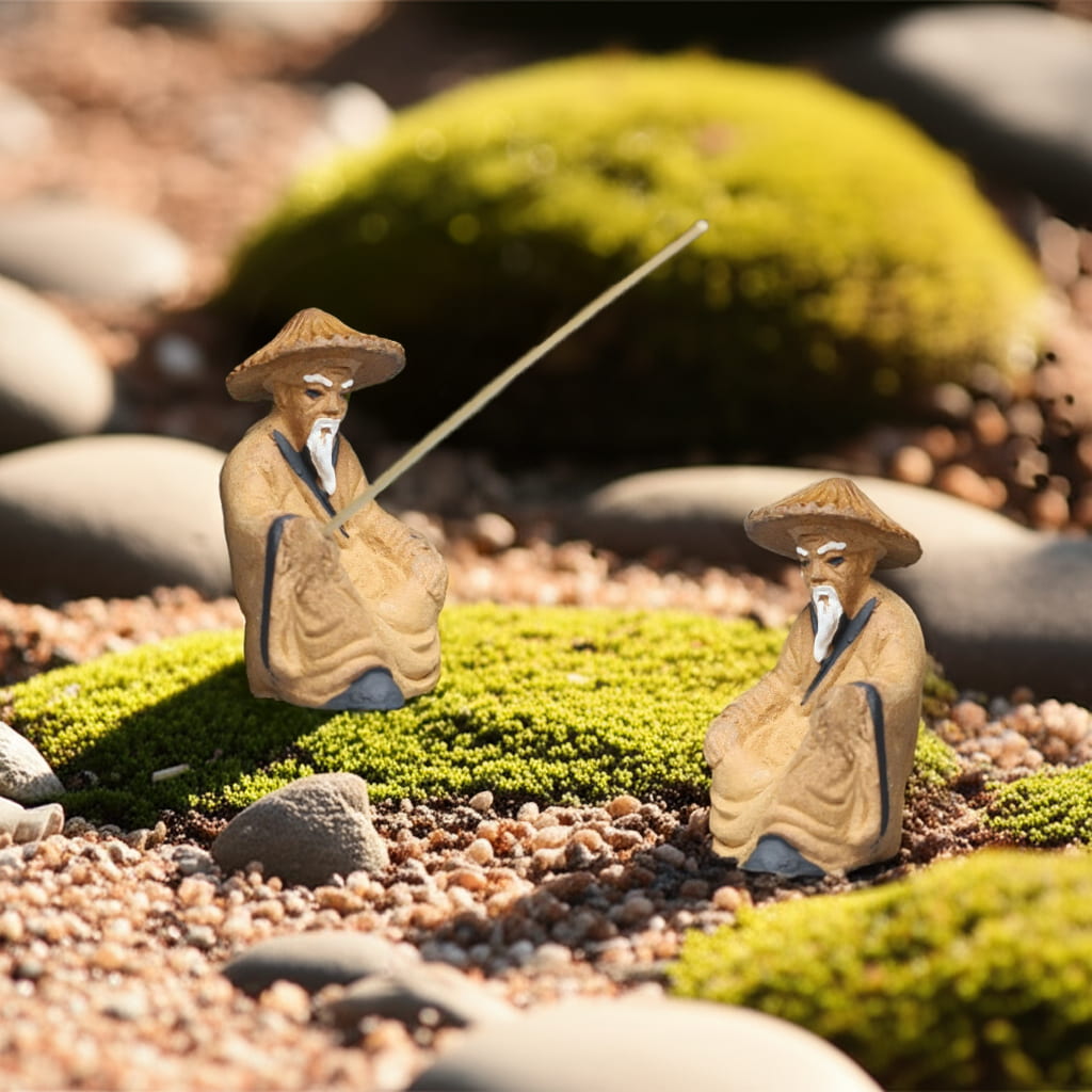 Two ceramic fisherman figurines, classic Bonsai Mudmen figurines, sit on mossy rocks.