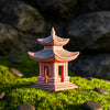 Close-up of a handcrafted ceramic pagoda with intricate pillar details and a weathered grey roof. The reddish-brown clay figurine rests on a mossy surface, designed as non-toxic ceramic aquarium decor or a bonsai accent.