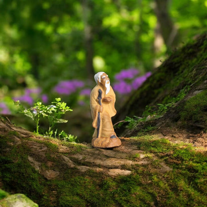  A small ceramic mudman figurine in a brown robe stands on a tree trunk.