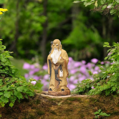 A small ceramic mudman figurine stands on a moss-covered tree trunk.