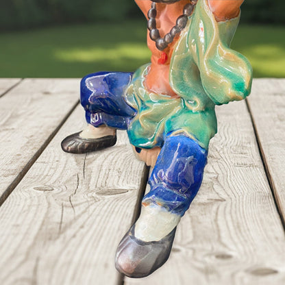A close-up of the glazed blue pants and green cloth of the ceramic figurine pot.