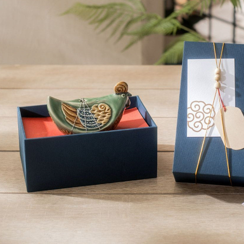 A green Vietnamese ceramic rooster figurine is nestled inside its dark blue and red gift box.