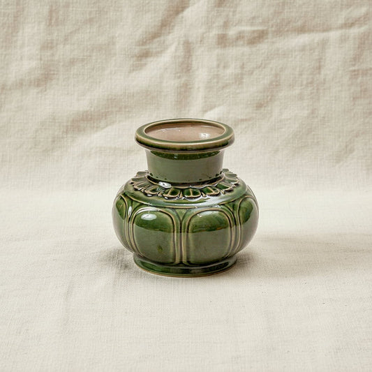 A green Vietnamese ceramic vase on a cream cloth. This low wide flower vase has embossed details.
