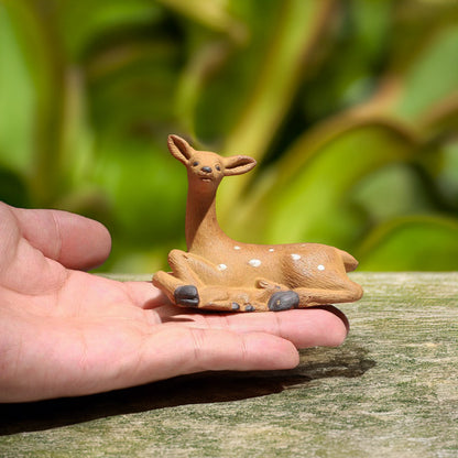 A tiny ceramic deer, hand-painted with delicate white spots, rests comfortably in the palm of a hand, showcasing the intricate detail of this miniature masterpiece.