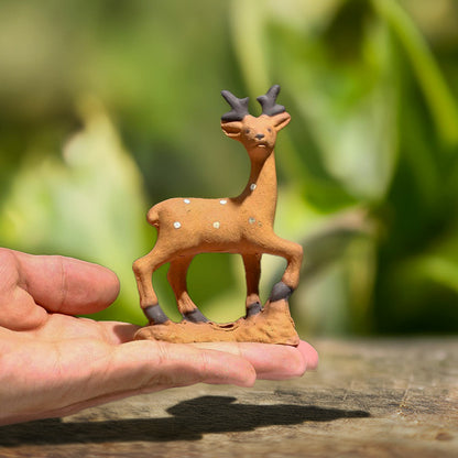 A tiny ceramic deer, meticulously handcrafted with delicate white spots and black horns, rests gently in a hand, showcasing the artistry of Vietnamese Bat Trang ceramics.