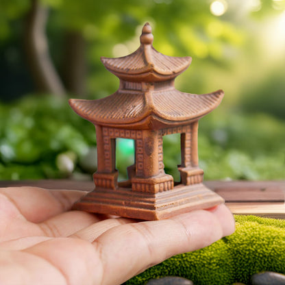 Another hand holds a slightly smaller brown clay pagoda statue. This miniature pagoda figurine has steps leading up to an opening. It's made from Bat Trang ceramic.