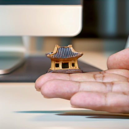 A hand holds a very small, brown miniature pagoda statue showing its tiny size. A detailed bonsai figurine.