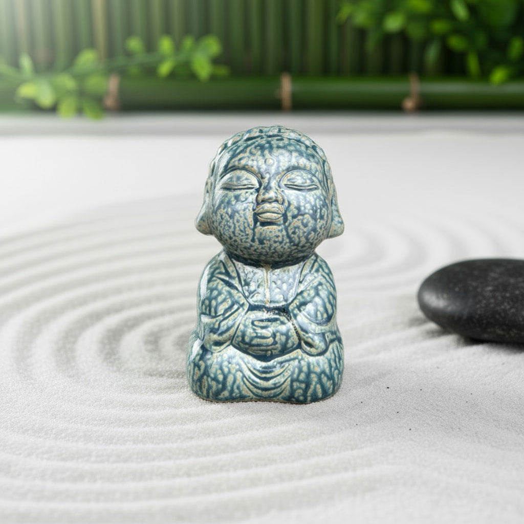 A blue crackle-glaze handmade buddha figurine on sand. A unique, artisanal buddha figurine.