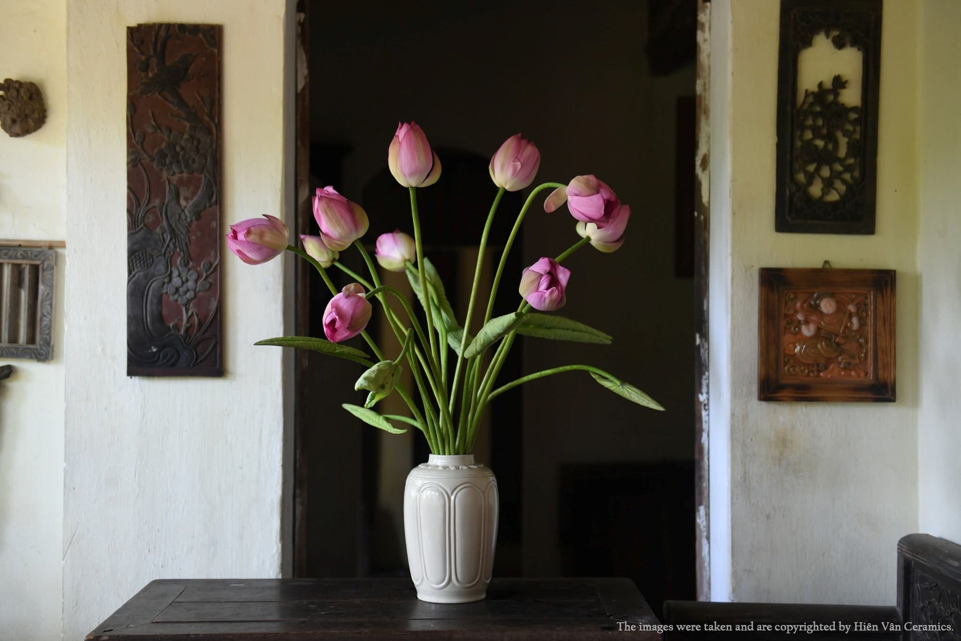 A white ash glaze vase holding pink lotus. This handmade vietnamese vase is on a dark table.