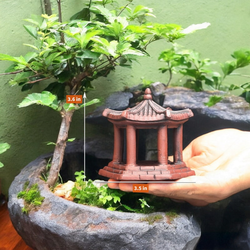 A person holding a miniature pagoda statue with a bonsai tree in the background.