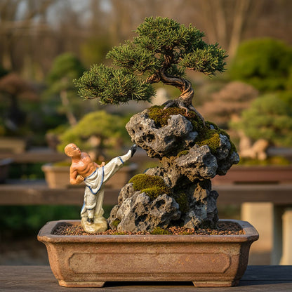 A martial artist bonsai figurine kicks a mossy rock next to a bonsai tree. Unique bonsai decor.