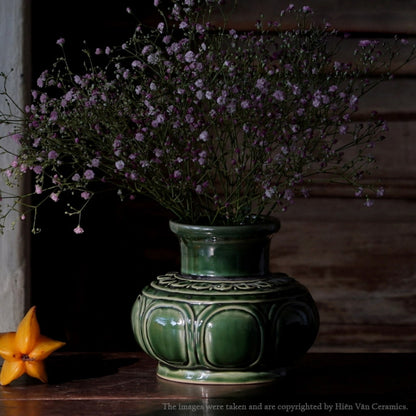  A green Vietnamese ceramic vase in low light. This low wide flower vase holds baby's breath.