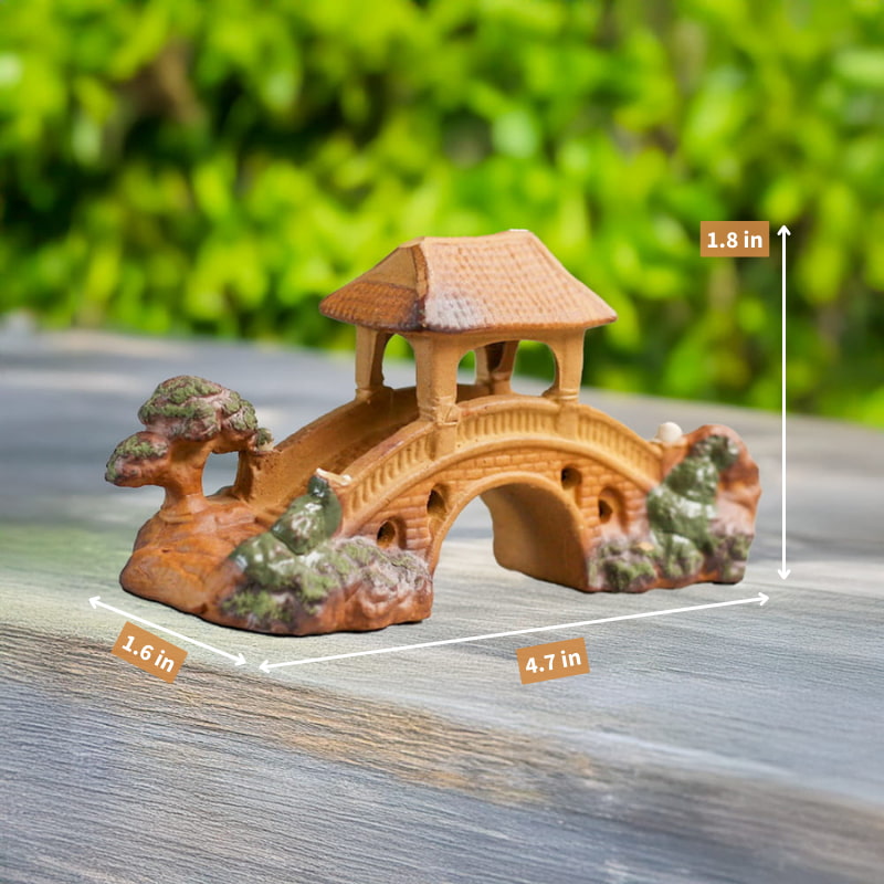 A small, brown ceramic miniature bridge with a pagoda-style roof rests on a wooden surface. Measurements indicating its length, width, and height are visible.