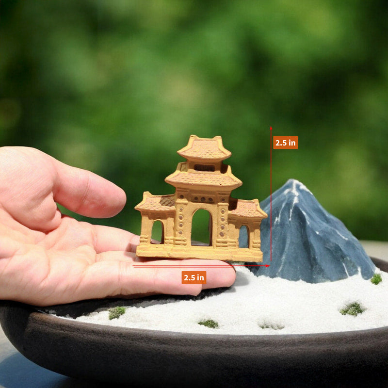 A person is holding a small yellow three entrance gate statue in their hand, next to a miniature mountain.