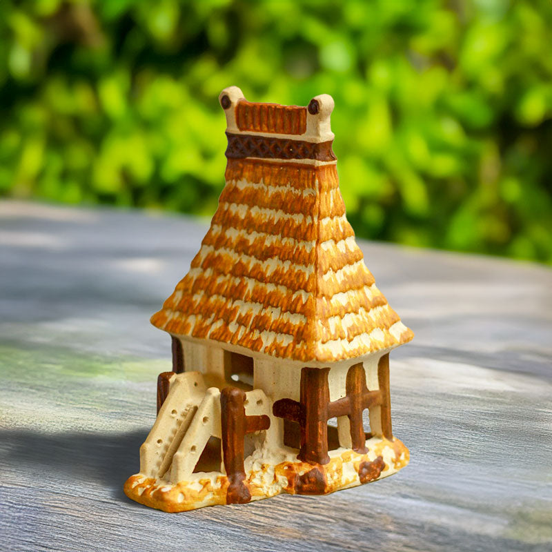 A beautifully handcrafted ceramic house, modeled after a traditional Vietnamese Rong house, stands invitingly amidst lush greenery, creating a captivating focal point in any terrarium.