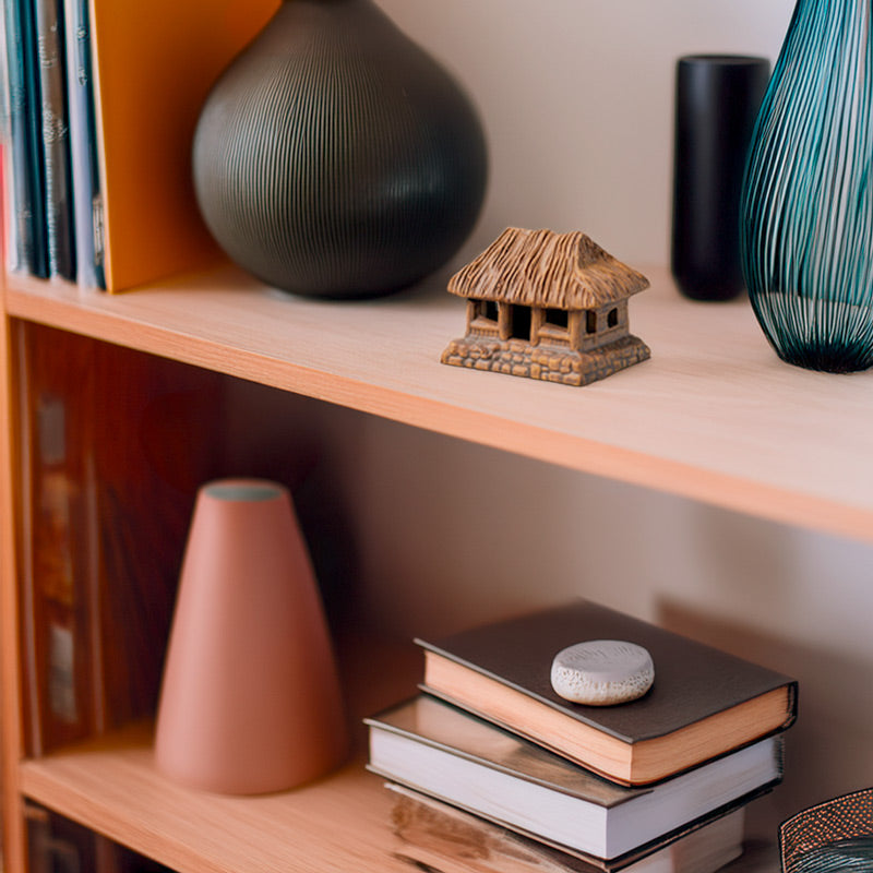 A miniature ceramic thatched house, nestled amongst books and decorative items on a bookshelf, adds a touch of rustic charm and Vietnamese heritage to any home.