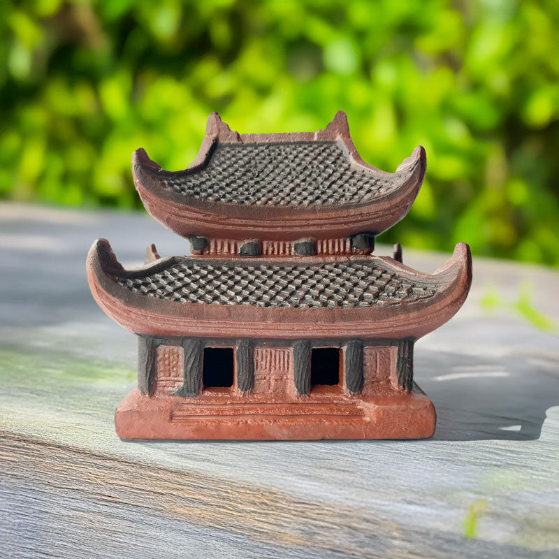 A miniature Vietnamese pagoda, crafted from earthy brown ceramic, stands serenely on a weathered wooden surface, evoking the tranquility of a Buddhist temple.