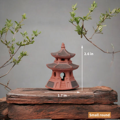 A small, round, red ceramic pagoda sits on a weathered wooden surface. Its two tiers and intricate details showcase traditional Japanese architecture.