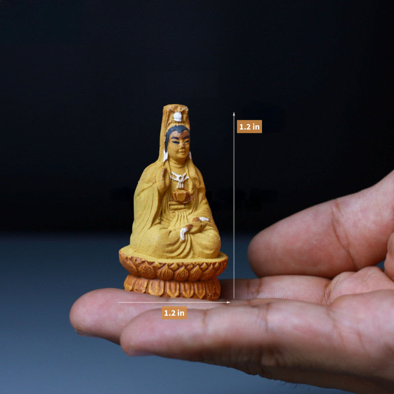 A small yellow Quan Yin figurine, held in a hand.