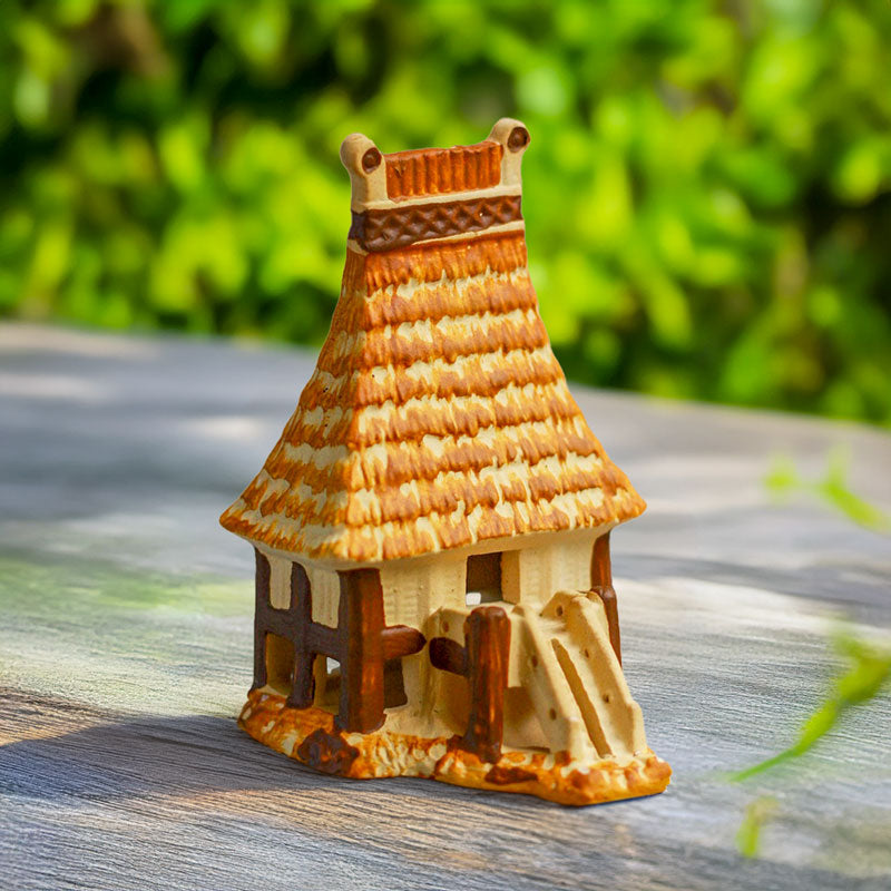 A miniature Vietnamese communal house, crafted from warm brown ceramic, with a distinctive thatched roof and intricate stilts, sits proudly on a wooden table.