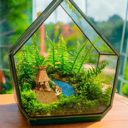 A miniature Vietnamese communal house, with its iconic stilts and thatched roof, sits peacefully beside a miniature pond, adding a touch of Southeast Asian artistry to this terrarium.