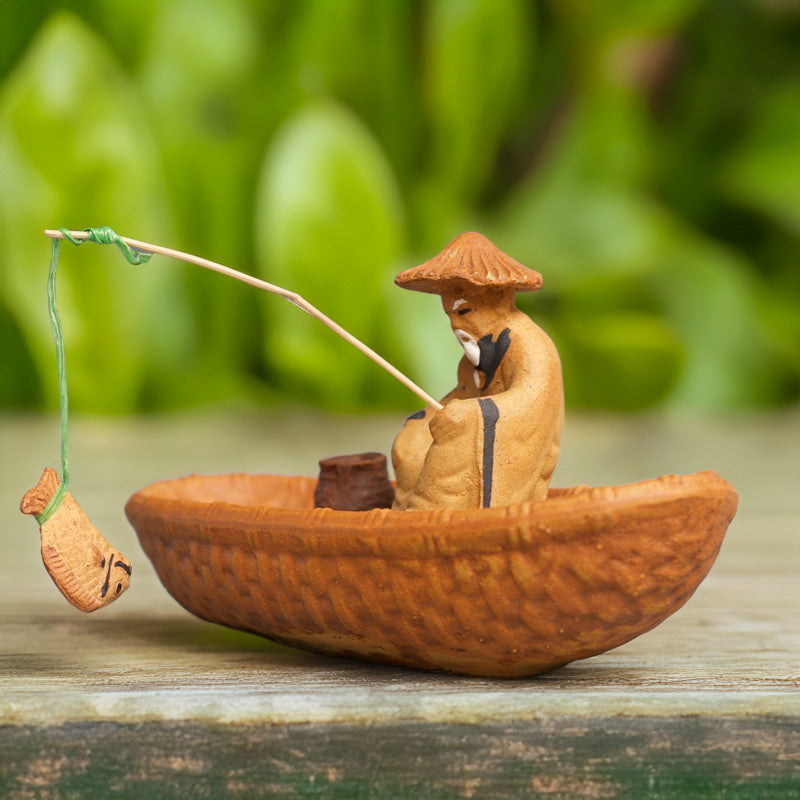 A miniature Vietnamese fisherman, clad in traditional attire, casts his line from a rustic ceramic boat, evoking a sense of tranquility and patience