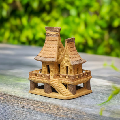 A miniature Vietnamese stilt house, crafted from warm-toned ceramic, with its iconic double roof and delicate stilts, perches charmingly on a wooden surface.