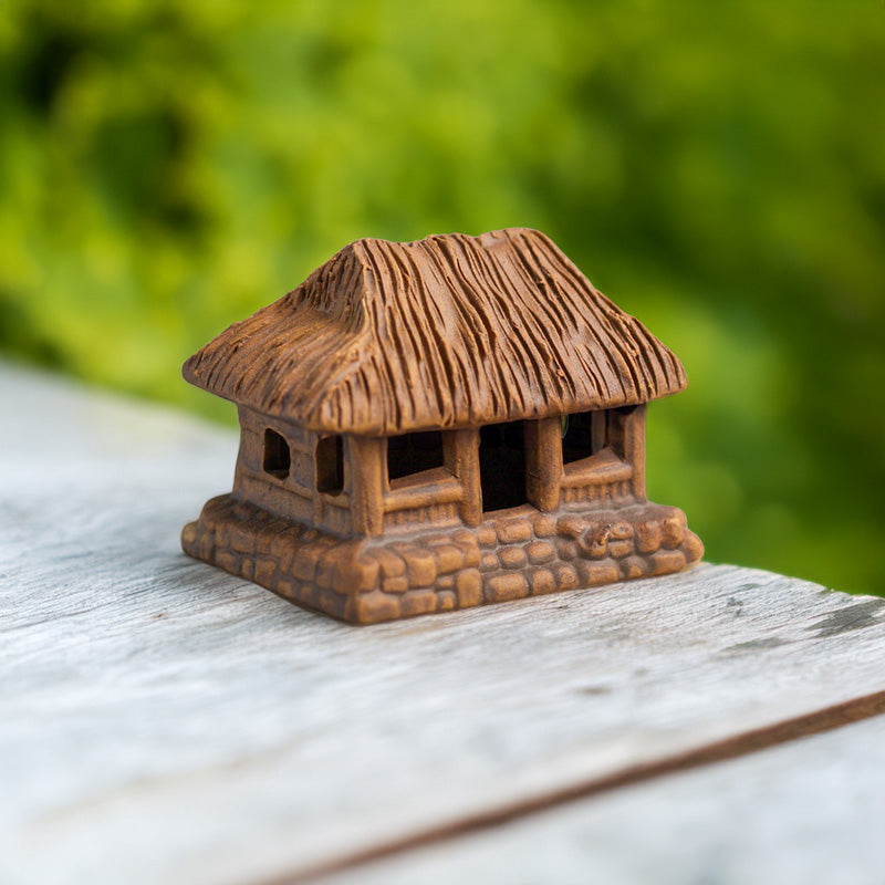  A charming miniature thatched house, crafted from rustic brown ceramic, sits peacefully on a wooden surface, bringing a touch of Vietnamese tradition to any space.