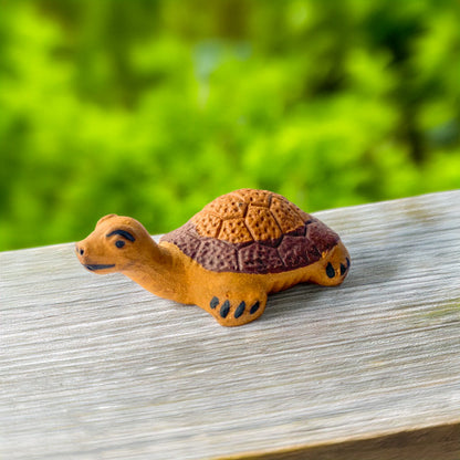 A small ceramic turtle, handcrafted in Vietnam, stretches its neck curiously, its earthy brown shell contrasting beautifully with the natural wood grain beneath it.