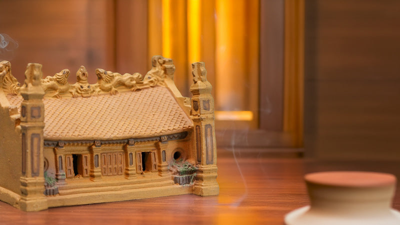  Incense smoke gently curls around a detailed miniature ceramic temple, handcrafted in Bat Trang, Vietnam, showcasing the intricate artistry of this traditional Vietnamese architecture.