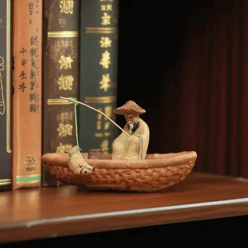 A miniature fisherman figurine in a boat sits on a shelf by books. This ceramic fisherman figure adds calm fisherman decor.