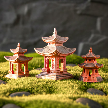 A collection of three different miniature pagoda styles arranged on a bed of green moss and dark pebbles. Each piece shows the unique reddish-brown texture of fired Hoang Tho clay, perfect for japanese pagoda decor and creating a peaceful zen garden decor.