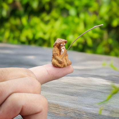 A miniature mudman, holding a delicate fishing rod, balances perfectly on a thumb, highlighting the miniature scale and exquisite craftsmanship of this unique figurine.