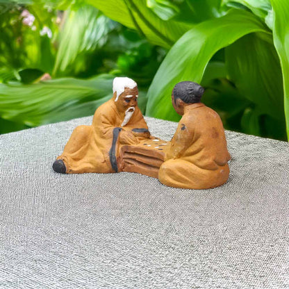 Two mudmen figurines, garbed in traditional earth-toned robes, engage in a friendly game of chess, adding a touch of serene wisdom to your miniature world.