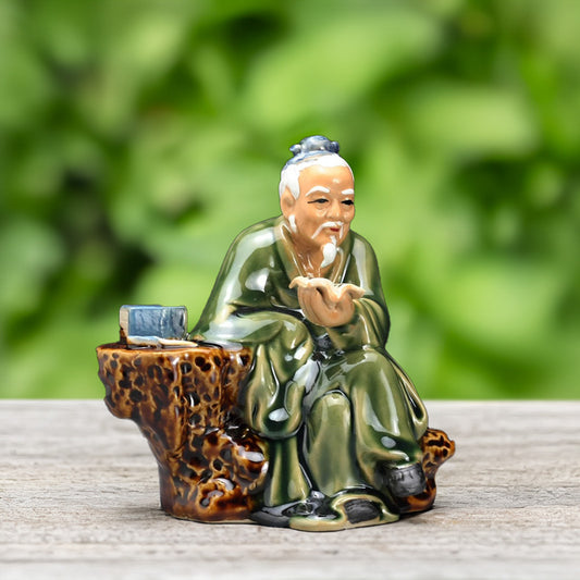 Perched on a rugged rock, a miniature old man figurine, his hand raised in contemplation, embodies the spirit of wisdom and serenity, bringing a touch of Zen to your bonsai.