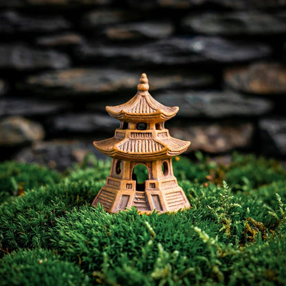 An ornate three-tier ceramic pagoda figurine with a circular base, nestled in green moss. This piece of Japanese decor is fired at high temperatures for lasting durability in terrariums or bonsai displays.